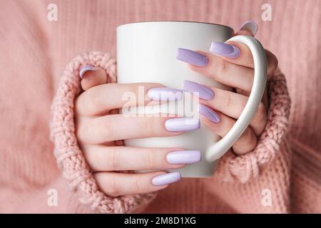 Trendige weibliche Maniküre. Frauenhände mit violetter Maniküre, die eine Tasse Tee halten. Gemütliches Winter- oder Herbstkonzept. Stockfoto