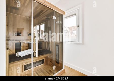 Ein Badezimmer mit Holzfußboden und weißen Wänden, es gibt eine gläserne Duschkabine in der Ecke rechts Stockfoto