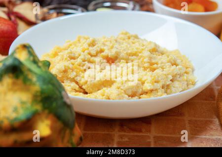 Kürbisbrei mit Hirse – traditionelle ukrainische Küche. Nahaufnahme Kürbisbrei mit Hirse, serviert in einer weißen Schüssel, selektiver Fokus. Stockfoto