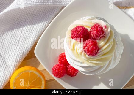 Blick von oben auf den weißen Mini-Baiser-Pavlova-Kuchen mit süßen rosa Himbeeren und Mascarpone Creme auf dem Teller in der Küche. Stockfoto