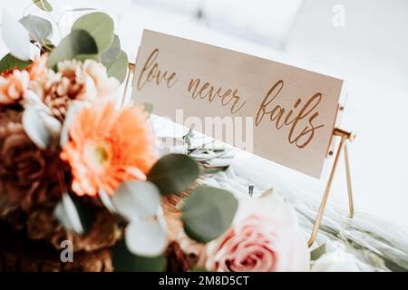 Eine dekorative LIEBE VERSAGT NIE auf einem hochzeitszettel mit einem floralen Herzstück Stockfoto