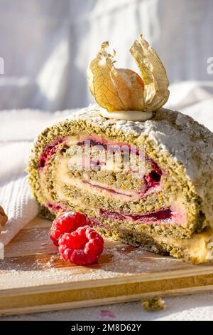 Grüne Pistazien-Baiser-Roulade mit Himbeermarmelade auf hellem Holzbrettgrund in der Küche. Stockfoto