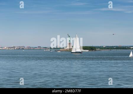 Segelboote auf dem hudson River, die an der berühmten Wahrzeichen-Freiheitsstatue auf ellis Island in New York vorbeifahren. Stockfoto