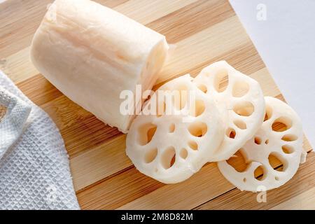 Weiße Lotuswurzel (Renkon) in Scheiben auf dem Holzschneidbrett in der Küche. Stockfoto