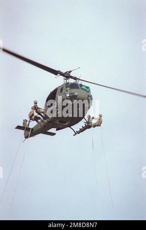 Vier Mitglieder von 4. Mrd., 22. Inf., 25. Inf. Div (Licht), stellen Sie sich auf die Kufen eines 53. Luftbataillons UH-1H Iroquois Helikopters, während sie auf ihre Abseilung warten. Die Schulung wird im Rahmen der kombinierten Thai/US-Übung Cobra Gold '90 durchgeführt. Betreff Operation/Serie: COBRA GOLD '90 Basis: Chon Buri Land: Thailand (THA) Stockfoto