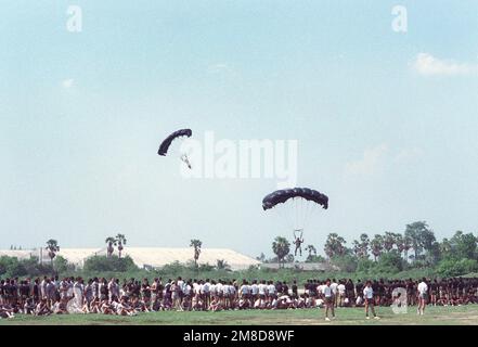 Thailändische Soldaten und Mitglieder von 4. Mrd., 22. Inf., 25. Inf. Div (Licht) beobachten Sie, wie zwei Fallschirmspringer eine Demonstration als Teil eines „Sporttags“ durchführen, der während der kombinierten Thai/US-Übung Cobra Gold '90 in einem thailändischen Armeelager stattfindet. Betreff Operation/Serie: COBRA GOLD '90 Basis: Chon Buri Land: Thailand (THA) Stockfoto