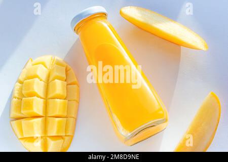 Draufsicht auf leuchtend gelben Mangosaft in einer Glasflasche mit geschnittenen frischen Mangos auf weißem Hintergrund Nahaufnahme. Stockfoto