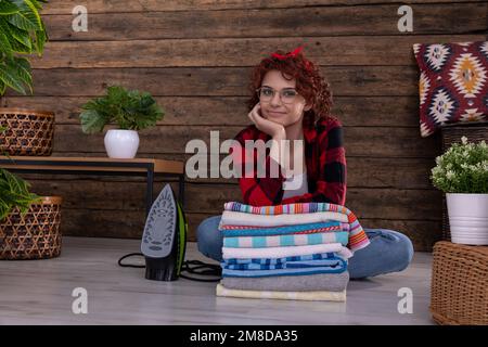 Das Mädchen sitzt auf dem Boden und lehnt sich auf frisch gewaschene und gebügelte Handtücher. Stockfoto