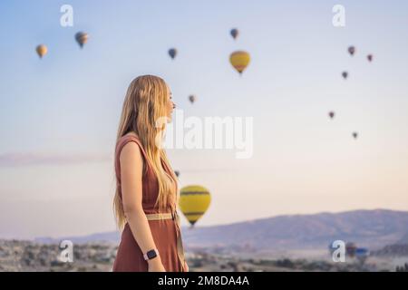 Eine Touristin, die Heißluftballons in Kappadokien, Türkei, ansieht. Happy Travel in Turkey Concept. Eine Frau auf einem Berggipfel, die eine wunderbare Aussicht genießt Stockfoto