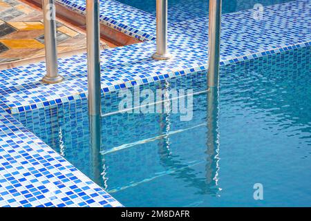 Eine Metall Swimming Pool Safe Leiter (Skimmer) am Eingang zum Haus auf der Poolseite mit dem blauen sauberen Wasser. Stockfoto