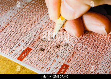 Nahaufnahme der Hand einer Person, die Lottozahlen auswählt und markiert, mit einem Bleistift auf dem Lottospielzettel. Stockfoto