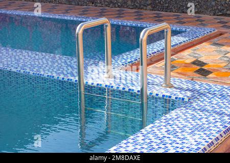 Eine Metall Swimming Pool Safe Leiter (Skimmer) am Eingang zum Haus auf der Poolseite mit dem blauen sauberen Wasser. Stockfoto