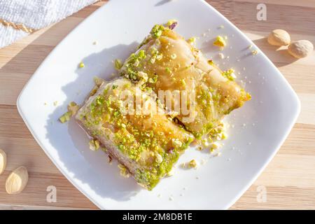 Blick von oben auf traditionelle ostasiatische süße gebackene Bahlava oder Pahlava mit Nüssen und Sirup auf einem weißen Teller auf hellem Holzhintergrund. Stockfoto