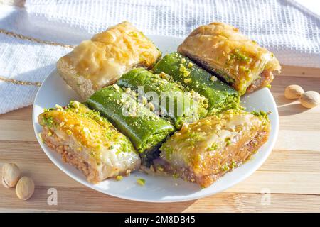 Traditionell ostasiatische süße gebackene Bahlava oder Pahlava mit Nüssen und Sirup auf einem weißen Teller mit hellem Holzhintergrund. Stockfoto