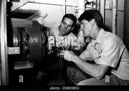 Elektriker-Mate 2. Klasse Mark Davis, Left, „Sailor of the Year“ für die mittelgroße schwimmende Trockendock-STÜTZE (AFDM-7), sieht zu, wie einer der Petty Officers in seinem Bereich einen Spannungsprüfer zur Überprüfung eines Generators verwendet. Basis: Marine Air Station, Norfolk Bundesstaat: Virginia (VA) Land: Vereinigte Staaten von Amerika (USA) Stockfoto