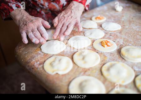 Menschliche Hände zum Füllen und Versiegeln von Blätterteigknödeln. Küche. Stockfoto