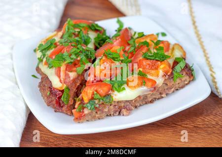 Leckere hausgemachte Low-Carb Keto Meatza (Getreide- und glutenfreie Pizza auf Rindfleischbasis) mit Gemüse und Mozzarella-Käse auf einer weißen Holzplatte Stockfoto