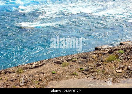 Schneller, klarer, blauer Fluss mit Wellen, die im Sommer in der Nähe der felsigen Küste fließen. Stockfoto