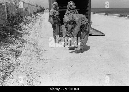 Zwei Mitglieder des 71. Chemiegiments, 25. Infanterie-Division (Light), tragen eine komplette Schutzausrüstung und sehen, wie ein dritter Soldat mit einem Chemieüberwachungsgerät auf Verunreinigungen in der Nähe einer Containerschachtel (CONEX) überprüft, in der chemische Munition gelagert wird. Die Soldaten nehmen an einer Übung Teil, um die Fähigkeit der Einheit zu testen, ein chemisches Leck zu erkennen und zu mindern. Basis: US Army Chemical Activity Country: Johnston Atoll Stockfoto