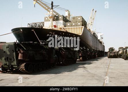 Amphibienfahrzeuge der Marine AAVP-7A1, Gabelstapler und Baugeräte säumen den Pier neben dem Schiff PFC für die Vorpositionierung. Dewayne T. Williams (T-AK-3009) während der Operation Desert Shield. Betreff Operation/Serie: WÜSTENSCHILD Land: Saudi-Arabien (Sau) Stockfoto