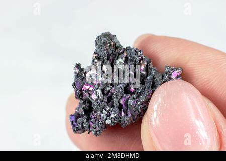 Weibliche Hand mit glänzendem schwarzem Carborundkristall (Moissanit oder Siliziumkarbid) auf heller Nahaufnahme des Hintergrunds. Stockfoto