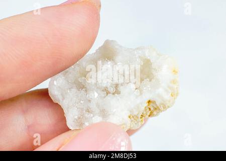 Weibliche Hand, die glänzende weiße Kristall-Agate auf hellen Hintergrund-Nahaufnahmen hält. Stockfoto