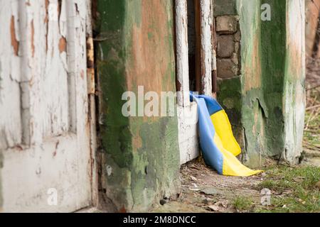 Ein zerstörtes Wohngebäude und die Flagge der Ukraine liegen auf den Ruinen des Hauses, dem Krieg und dem Beschuss russischer Wohngebäude Stockfoto