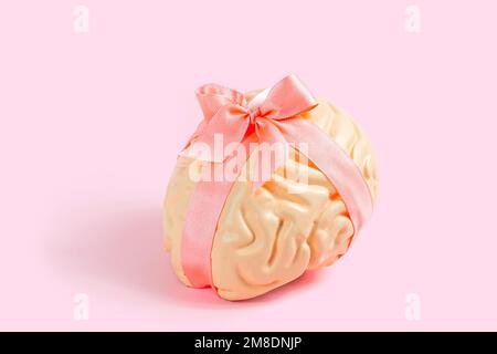Leuchtend pinkfarbenes menschliches Hirnmodell mit Satinschleife auf pastellfarbenem Hintergrund. Kreativität, Inspiration und psychisches Gesundheitskonzept. Stockfoto