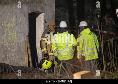 Erkelenz, Deutschland. 13. Januar 2023. Feuerwehrleute und Spezialisten von RWE stehen am dritten Tag der Evakuierung des Braunkohlendorfes Lützerath, das von Klimaktivisten besetzt war, vor dem Eingang zu einem Gebäude. Hier sollen sich Aktivisten in einem Tunnel verbarrikadiert haben. Das Energieunternehmen RWE will die unter Lützerath liegende Kohle ausheben - zu diesem Zweck soll das Weiler auf dem Gebiet der Stadt Erkelenz am Braunkohlebergwerk Garzweiler II abgerissen werden. Kredit: Thomas Banneyer/dpa/Alamy Live News Kredit: dpa Picture Alliance/Alamy Live News Stockfoto
