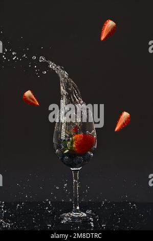 Mehrere Erdbeeren fallen in ein Glas und spritzen Wasser. Künstliche Einstellung Stockfoto