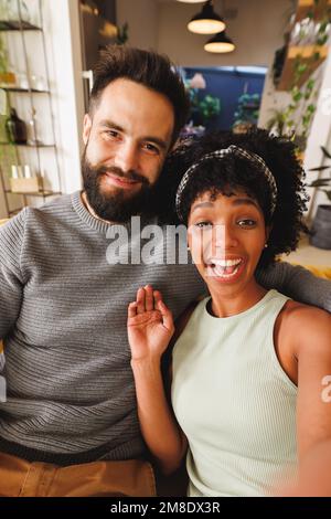 Porträt einer fröhlichen, birassischen Frau mit Afro-Haaren, die lacht, während sie mit ihrem Freund auf dem Sofa sitzt Stockfoto