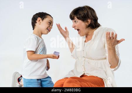 Ein kleiner Junge überrascht seine Mutter mit einem Geschenk. Muttertagskonzept. Studio-Bild mit weißem Hintergrund. Stockfoto