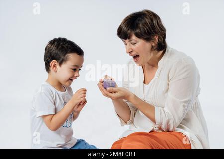 Alles gute zum Muttertag! Der Sohn gratulierte seiner mutter und schenkte ihr ein Geschenk. Studioporträt auf weißem Hintergrund Stockfoto
