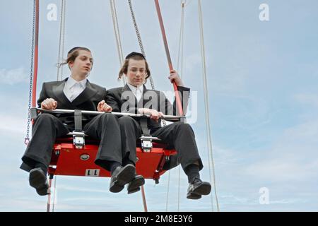 An einem Zwischentag des Sukkot-Urlaubs fahren orthodoxe jüdische Jungs mit langem Peyot auf dem Brooklyn Flyer in Luna Park, Coney Island, Brooklyn. Stockfoto