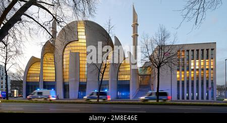 Köln, Deutschland, 11. Januar 2023: Schnelle Polizeiautos mit Bewegungsunschärfe und blauen Lichtern, die in der Abenddämmerung an der beleuchteten kölner Moschee blinken Stockfoto