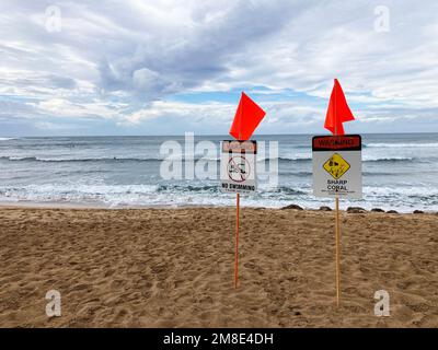 Zwei Warnschilder, scharfe Korallen, kein Schwimmen und rote Warnflaggen an einem beliebten Surfplatz am Haleiwa Beach auf Oahu Hawaii während des Wintersturms. Stockfoto
