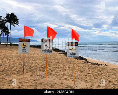 Drei Warnschilder, scharfe Korallen, kein Schwimmen, starke Strömung und rote Warnflaggen an einem beliebten Surfplatz am Haleiwa Beach auf Oahu Hawaii Dura Stockfoto
