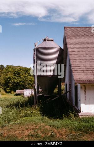 Ein Silo aus Metallkorn hinter einem weißen Hühnerstall an einem sonnigen Tag auf den Codman Community Farms. Lincoln, Massachusetts. Das Bild wurde analog aufgenommen Stockfoto