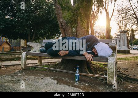Obdachloser oder Alkoholiker, der auf einer Bank schläft. Der arme Mann auf der Straße. Stockfoto