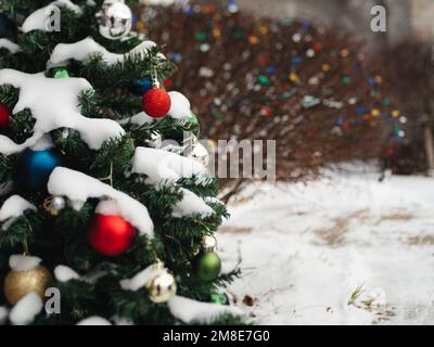 Schneebedeckter immergrüner Baum mit weihnachtskugeln draußen dekoriert. Stockfoto