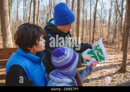 Ein Vater und Kinder stehen im Winter im Wald und schauen auf die Karte Stockfoto