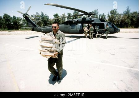 Ein Soldat trägt Zeitungen für US-Truppen, während seine Begleiter während der Operation Desert Shield Vorräte aus einem UH-60 Black Hawk (Blackhawk) Hubschrauber entladen. Betreff Operation/Serie: WÜSTENSCHILD Land: Saudi-Arabien (Sau) Stockfoto