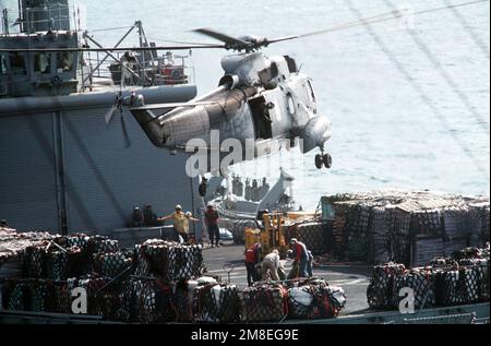 Besatzungsmitglieder an Bord des Kampfladenschiffs USS NIAGARA FALLS (AFS-3) befestigen mehrere Bündel an einer Linie, die während der Operation Desert Storm von einem SH-3H Sea King Helikopter über dem Flugdeck des Schiffs herabgesenkt wurde. Betroffene Operation/Serie: WÜSTENSTURM Land: Unbekannt Stockfoto