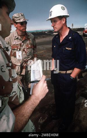 CHIEF PETTY Officer Keith Lebling und Journalist 2. Klasse Pete Hatzakos, beide vom Navy Broadcasting Service, interviewen CAPT. G.B. McEwen, kommandierender Offizier des amphibischen Angriffsschiffs USS TRIPOLI (LPH-10), bezüglich Schäden am Schiff. Die TRIPOLIS, die sich jetzt im Trockendock befinden und auf Reparaturen warten, wurde von einer irakischen Mine beschädigt, die das Schiff am 18. Februar während der Operation Desert Storm als Minenräumplattform im nördlichen Persischen Golf traf. Die TRIPOLIS konnte den Betrieb fortsetzen, nachdem die Schadenskontrollteams die durch die Explosion verursachten Überschwemmungen gestoppt hatten. Betreffbetrieb/Serie: D Stockfoto