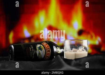 KIEW, UKRAINE - 4. MAI 2022 Baileys Original-Alkoholflasche auf Holztisch mit rotem Kamin im Hintergrund. Elite-Alkoholproduktion Stockfoto