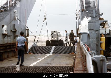 Ein Besatzungsmitglied steht bereit, um den Fahrer eines Gabelstaplers an Bord des Panzerlandeschiffs USS MANITOWOC (LST-1180) zu führen. Das Schiff transportiert zur Unterstützung der Operation Desert Shield Personal und Ausrüstung des Marine Corps nach Saudi-Arabien. Betreff Betrieb/Serie: WÜSTENSCHILD Bundesstaat: North Carolina (NC) Land: Vereinigte Staaten von Amerika (USA) Stockfoto