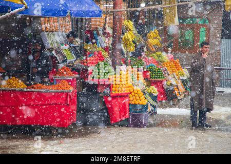 Srinagar, Indien. 12. Januar 2023. Ein Obstverkäufer wartet auf Kunden inmitten von anhaltendem starkem Schneefall in den Außenbezirken von Srinagar. Mindestens zwei Arbeiter wurden am Donnerstag getötet, nachdem eine Lawine in die Höhenlage in der Sonamarg im Zentrum Kaschmirs geriet. Die meisten Teile Kaschmirs erlitten einen frischen Schneefall, der zur Schließung der Hauptstraße der Hauptstadt Kaschmir führte, die die umstrittene Region mit dem Rest Indiens verbindet. Die Flughafenbehörden haben den Flugbetrieb bis auf weiteres eingestellt, da es ständig Schneefall und schlechte Sicht gab. Kredit: SOPA Images Limited/Alamy Live News Stockfoto