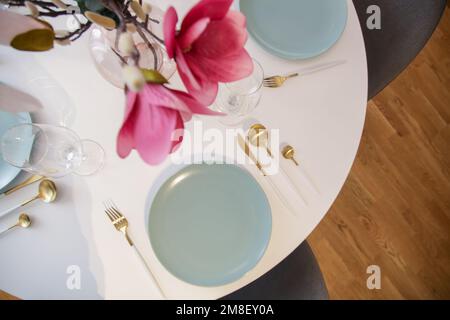 Runder Esstisch im modernen Apartment, Tischbestuhlung mit Blumen für eine zwanglose Dinnerparty. Stockfoto