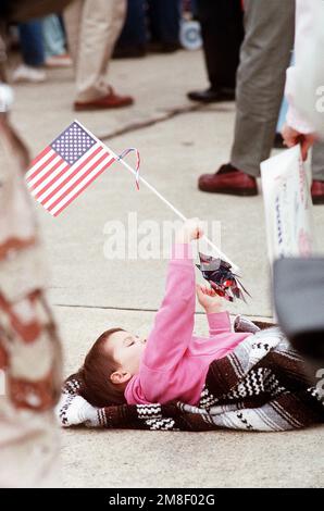 Ein Kind spielt mit einer Flagge, während es an einer Zeremonie zu Ehren von drei Offizieren der Marine teilnimmt, die vom Irak als Kriegsgefangene (Kriegsgefangene) festgehalten wurden. Die drei Marineflieger - LT. Robert Wetzel, LT. Jeffrey Zaun und LT. Lawrence Slade wurde während der Operation Desert Storm abgeschossen und gehörte zu der ersten Gruppe von zehn am 4. März freigelassenen Kriegsgefangenen der Koalition. Betreff Operation/Serie: STÜTZPUNKT WÜSTENSTURM: Marineflugstation, Oceana Bundesstaat: Virginia (VA) Land: Vereinigte Staaten von Amerika (USA) Stockfoto