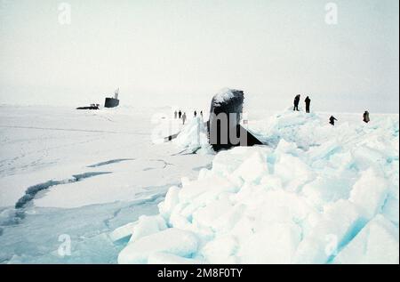 Besatzungsmitglieder stehen am Bug des nuklearbetriebenen Angriffs-U-Boots USS GURNARD (SSN-662), Hintergrund, während sich andere in der Nähe versammeln, um zu sehen, wie das nuklearbetriebene Angriffs-U-Boot USS SEAHORSE (SSN-669) während der Übung Ice Ex '90 durch das Eis taucht. Betrifft Operation/Serie: ICE EX '90 Land: Nordsee Stockfoto